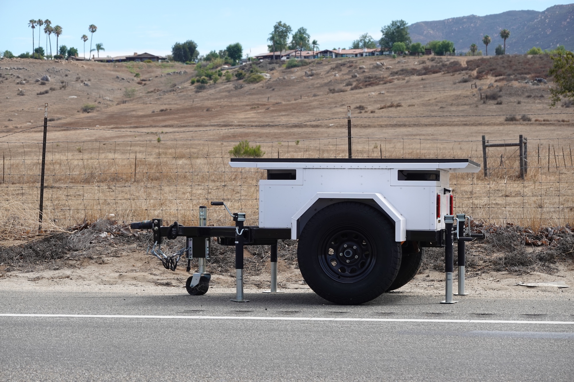 A white flat trailer by the side of the road with camera portals on either end. 